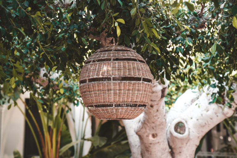 Geflochtene Kugellampe im Baum zwischen dichtem Grün.