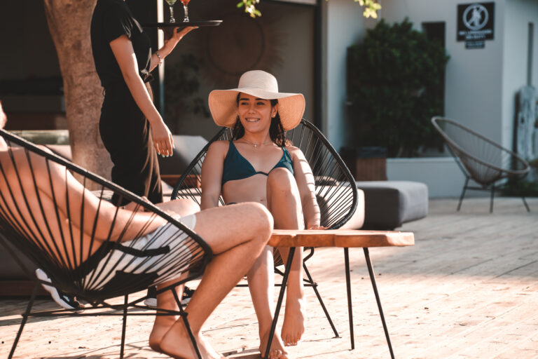 Entspannte Urlaubsszene mit Paar in Lounge-Stühlen und Cocktails auf Hotelterrasse.