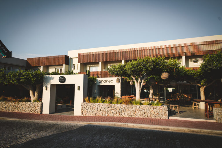 Außenansicht des modernen Hotelgebäudes ananea mit natürlicher Steinmauer, schattenspendenden Bäumen und stilvollem Eingangsbereich im minimalistischen Design bei Sonnenuntergang.