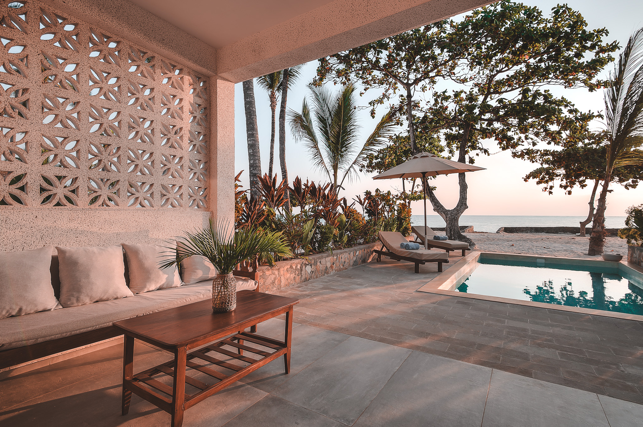 Überdachte Terrasse mit Sofa, Pool und Meerblick, eingerahmt von Palmen und tropischer Vegetation.