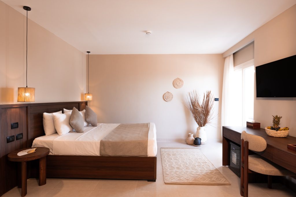 Modernes Hotelzimmer mit Doppelbett, Holzmöbeln, Deko aus Naturmaterialien und viel Tageslicht.