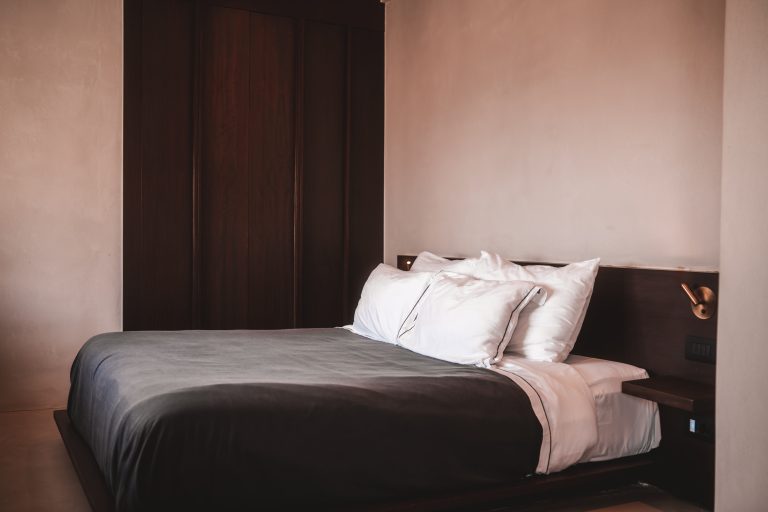 Minimalistisches Hotelzimmer mit Doppelbett, dunkler Holzverkleidung und schlichten weißen Kissen und Bettwäsche.