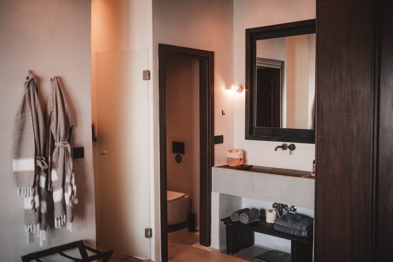 Modernes, stilvolles Badezimmer mit großem Spiegel, Waschbecken, Handtüchern und zwei Bademänteln an der Wand.