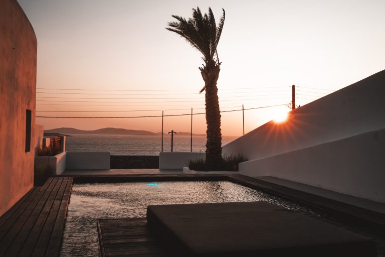 Privater Pool mit Holzdeck, Palme und Blick auf das Meer bei Sonnenuntergang auf Mykonos.