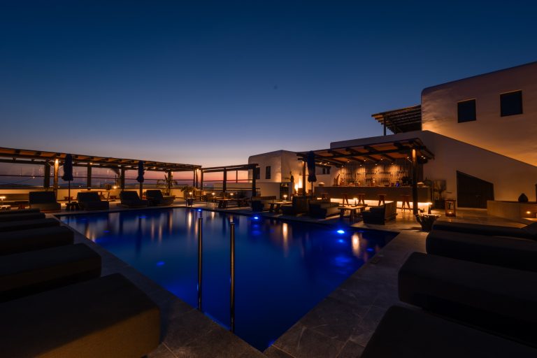 Luxuriöser Poolbereich mit Liegen und Bar auf Mykonos bei Sonnenuntergang, stimmungsvolle Beleuchtung am Abend.