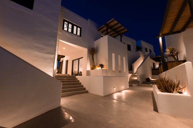 Beleuchtete, moderne Hotelanlage auf Mykonos in Weißtönen mit Treppen und Pflanzen bei Nacht.
