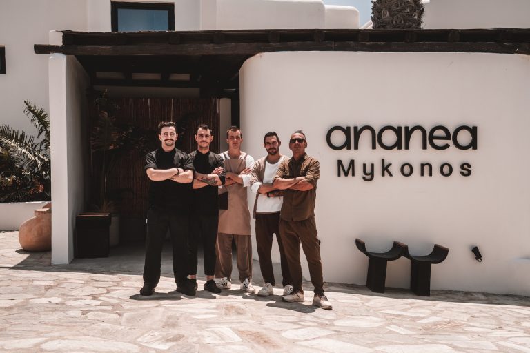 Fünf Mitarbeiter stehen vor dem Eingang des Ananea Mykonos Hotels und posieren lächelnd für ein Teamfoto in der Sonne.