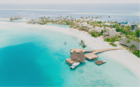 "Luxurious beach villas in the Maldives with palm trees, white sandy beaches, turquoise blue water and a wooden jetty with a pavilion leading into the sea."