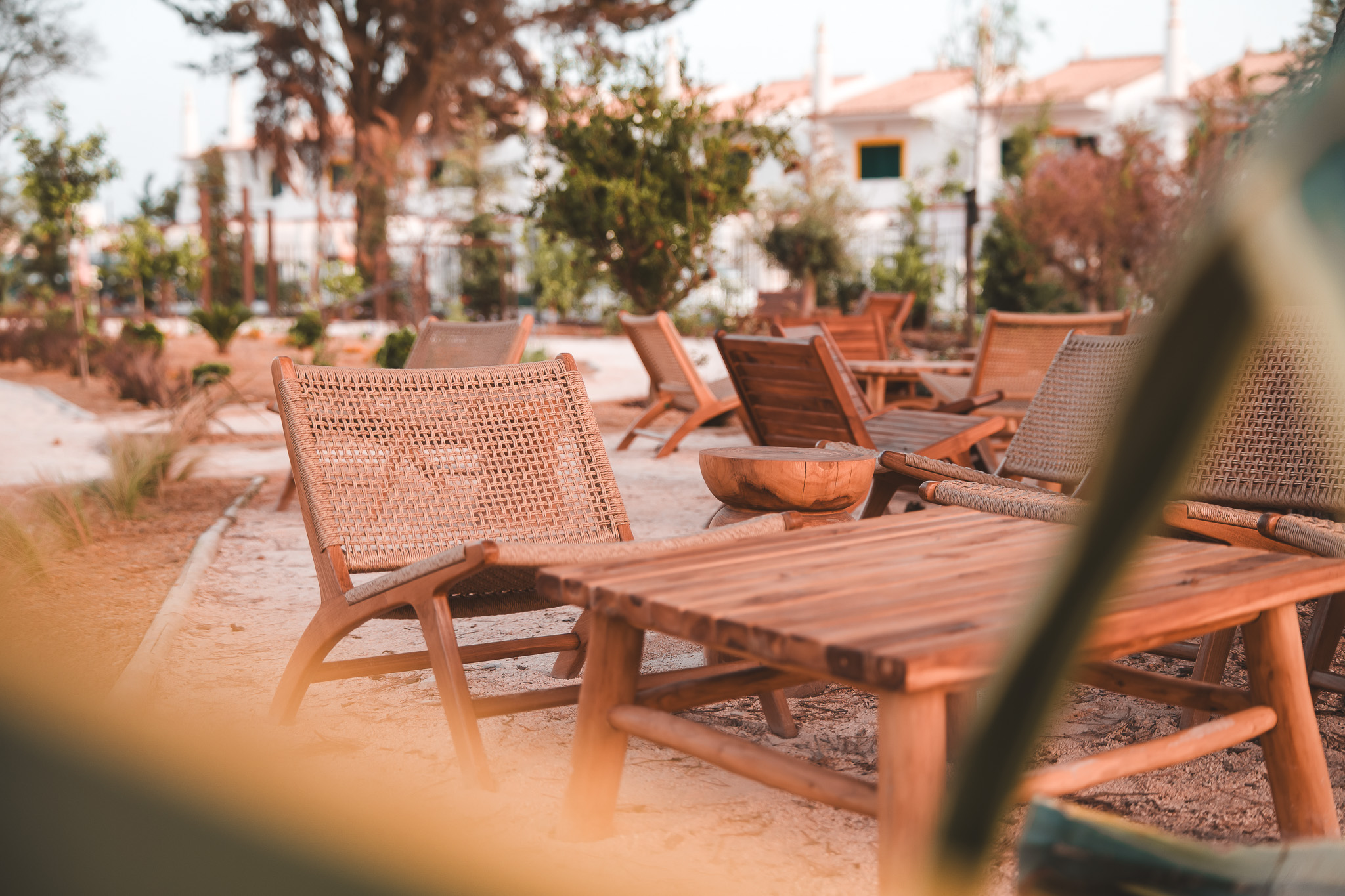 „Gemütliche Outdoor-Lounge mit Holztischen und geflochtenen Stühlen im Gartenbereich – entspannte Atmosphäre zum Verweilen unter freiem Himmel.“