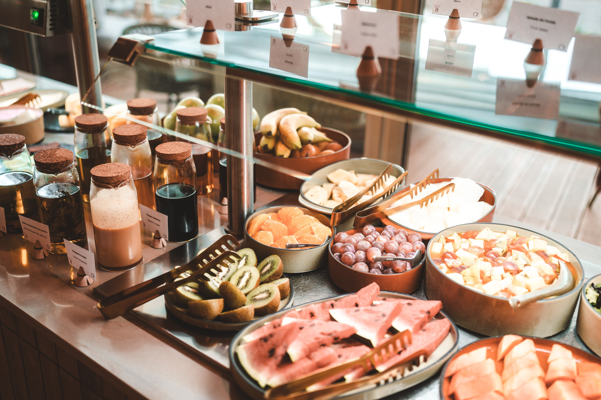„Frisches Frühstücksbuffet mit geschnittenem Obst wie Melonen, Trauben, Orangen und Kiwis sowie verschiedenen Säften in Gläsern.“