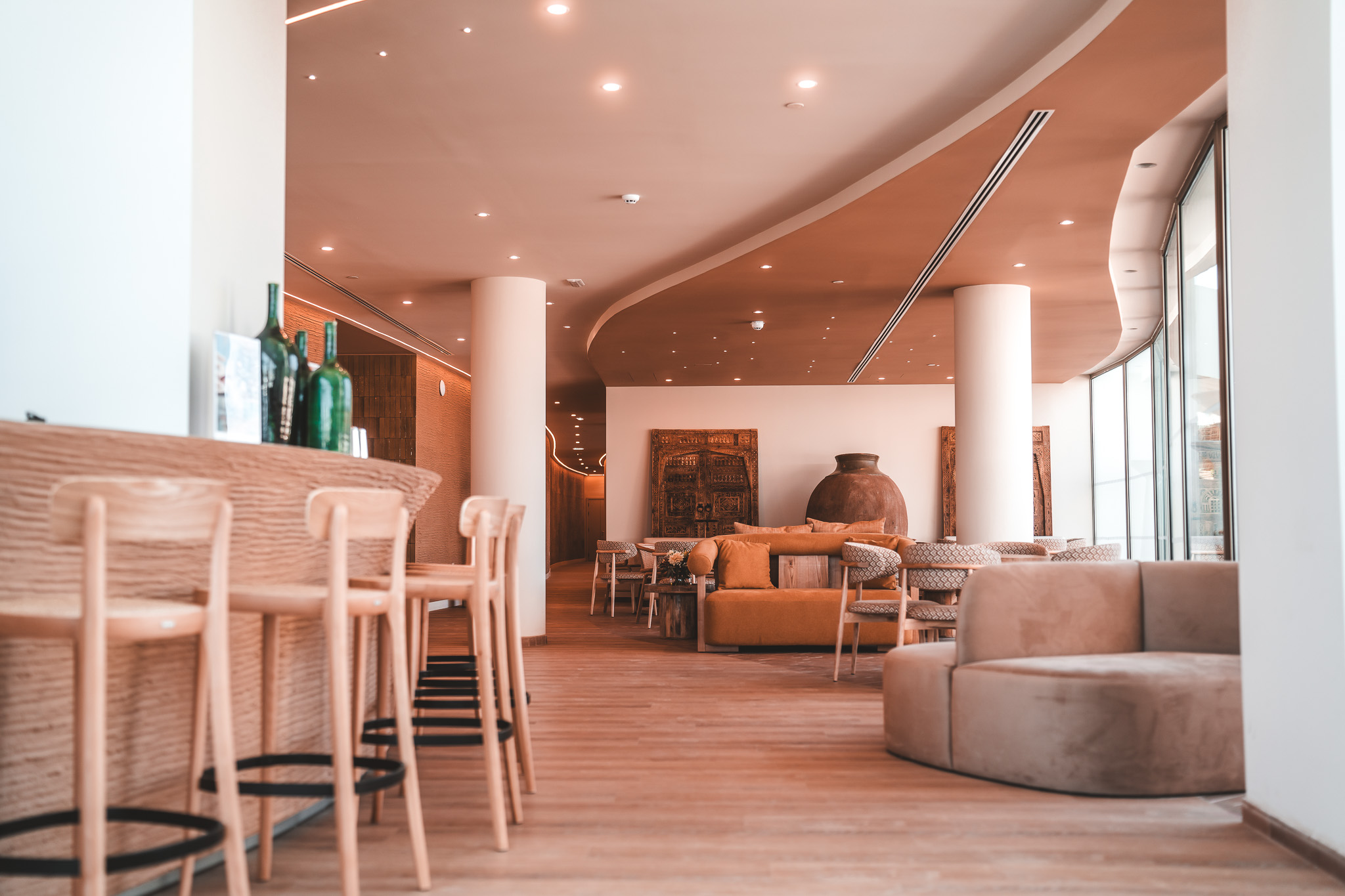 „Helle Lounge mit großen Glasfronten, modernen Sitzmöbeln und stilvollen Details, die eine warme und einladende Atmosphäre schaffen.“