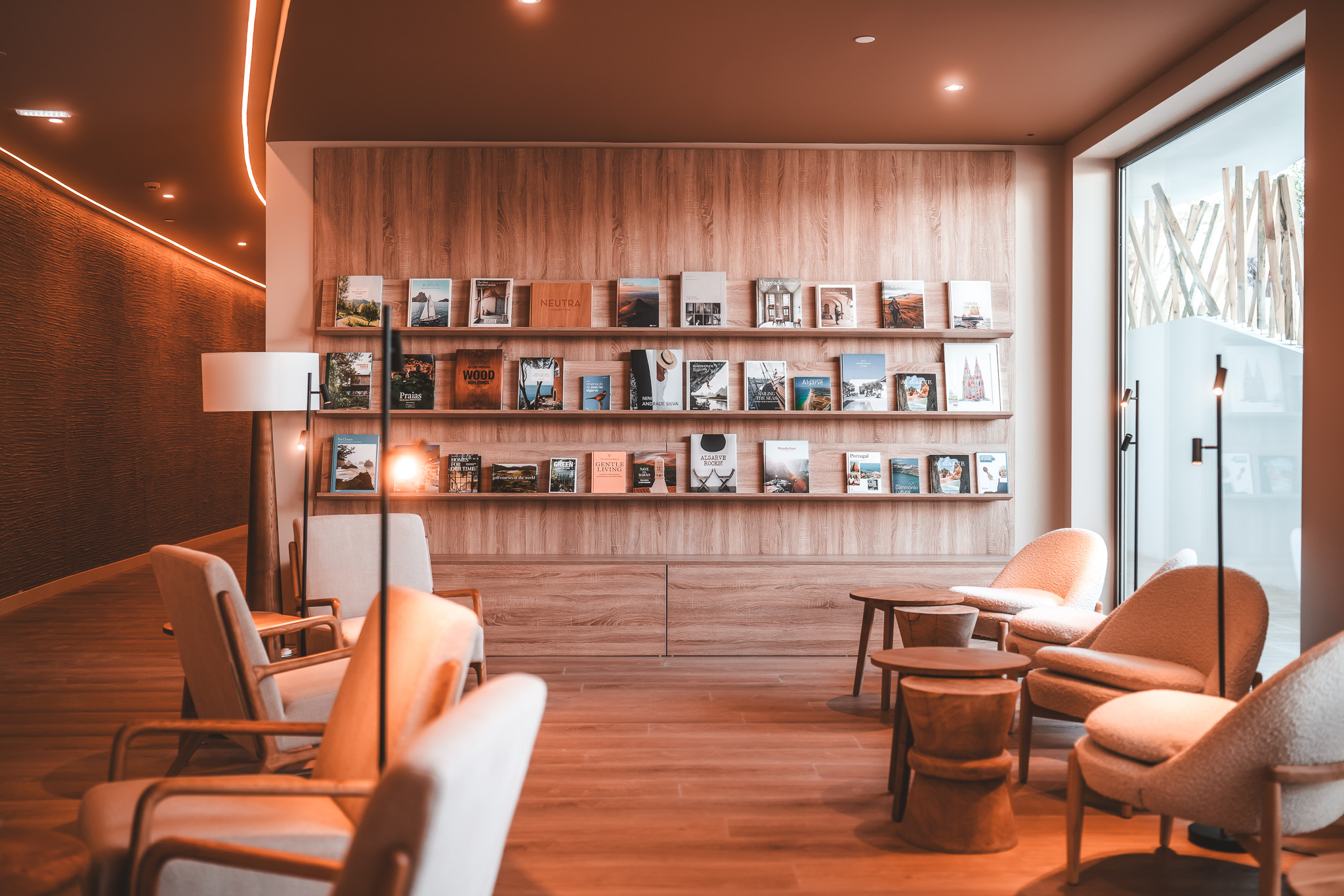 „Gemütliche Leseecke mit moderner Bücherwand, gefüllt mit Magazinen und Bildbänden, ergänzt durch stilvolle Sessel und warme Beleuchtung.“