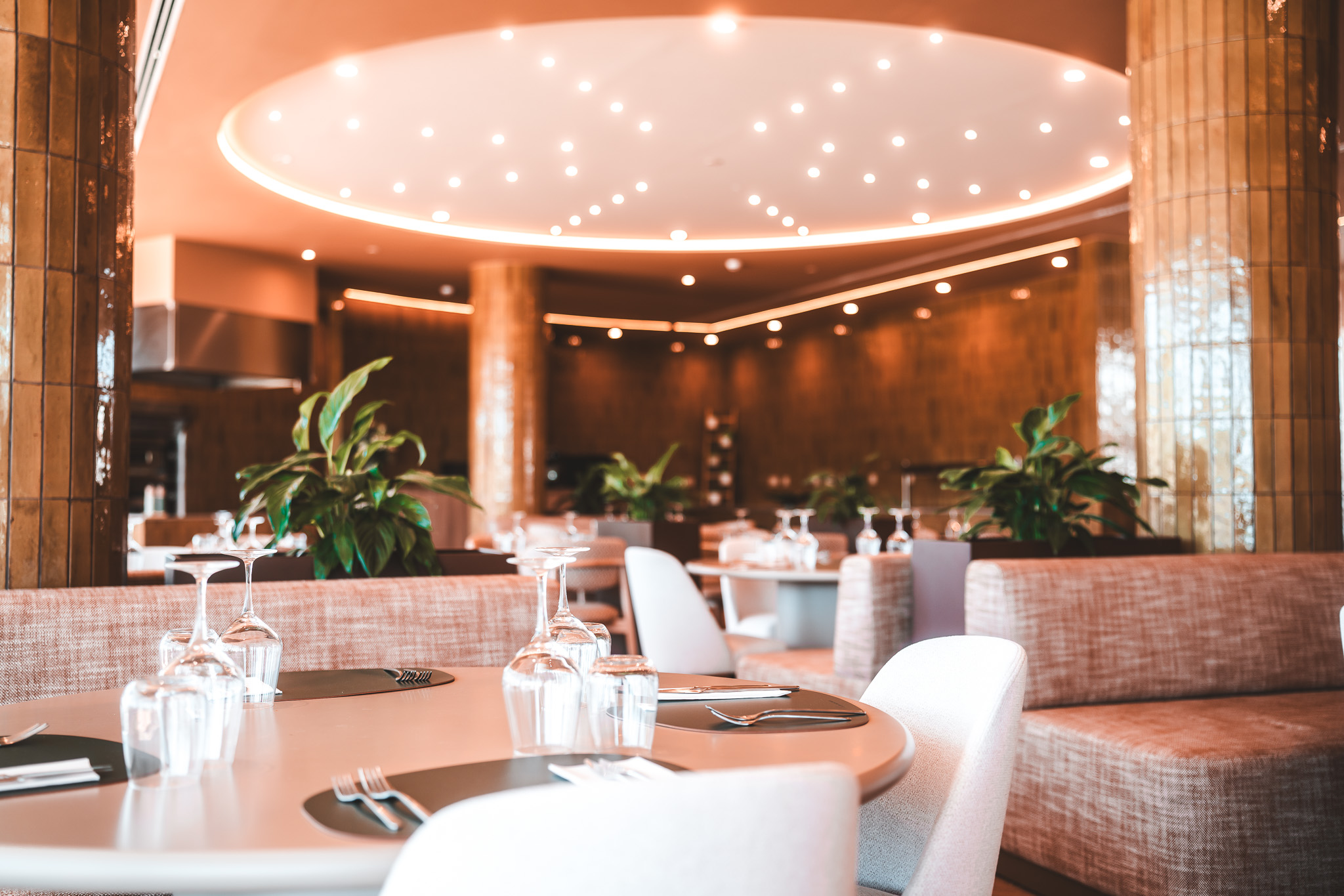 „Modernes Hotelrestaurant mit elegant gedeckten Tischen, stilvollen Sitzbereichen, warmem Lichtdesign und grünen Pflanzen für ein einladendes Ambiente.“