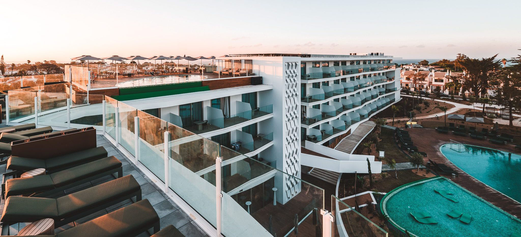 „Panoramablick auf das moderne Resort mit Pools, Sonnenterrassen und Rooftop-Bereich bei Sonnenuntergang – stilvolle Auszeit an der Algarve.“