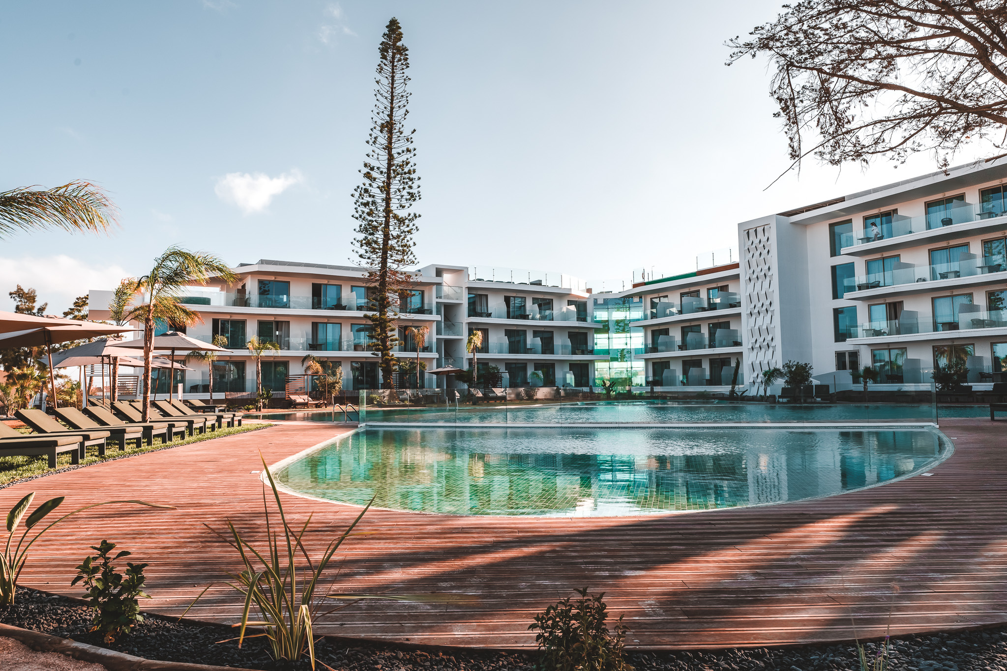 „Modernes Hotel mit Balkonzimmern, großer Poollandschaft, Sonnenliegen und Palmen unter blauem Himmel – perfekte Kulisse für einen entspannten Urlaub.“