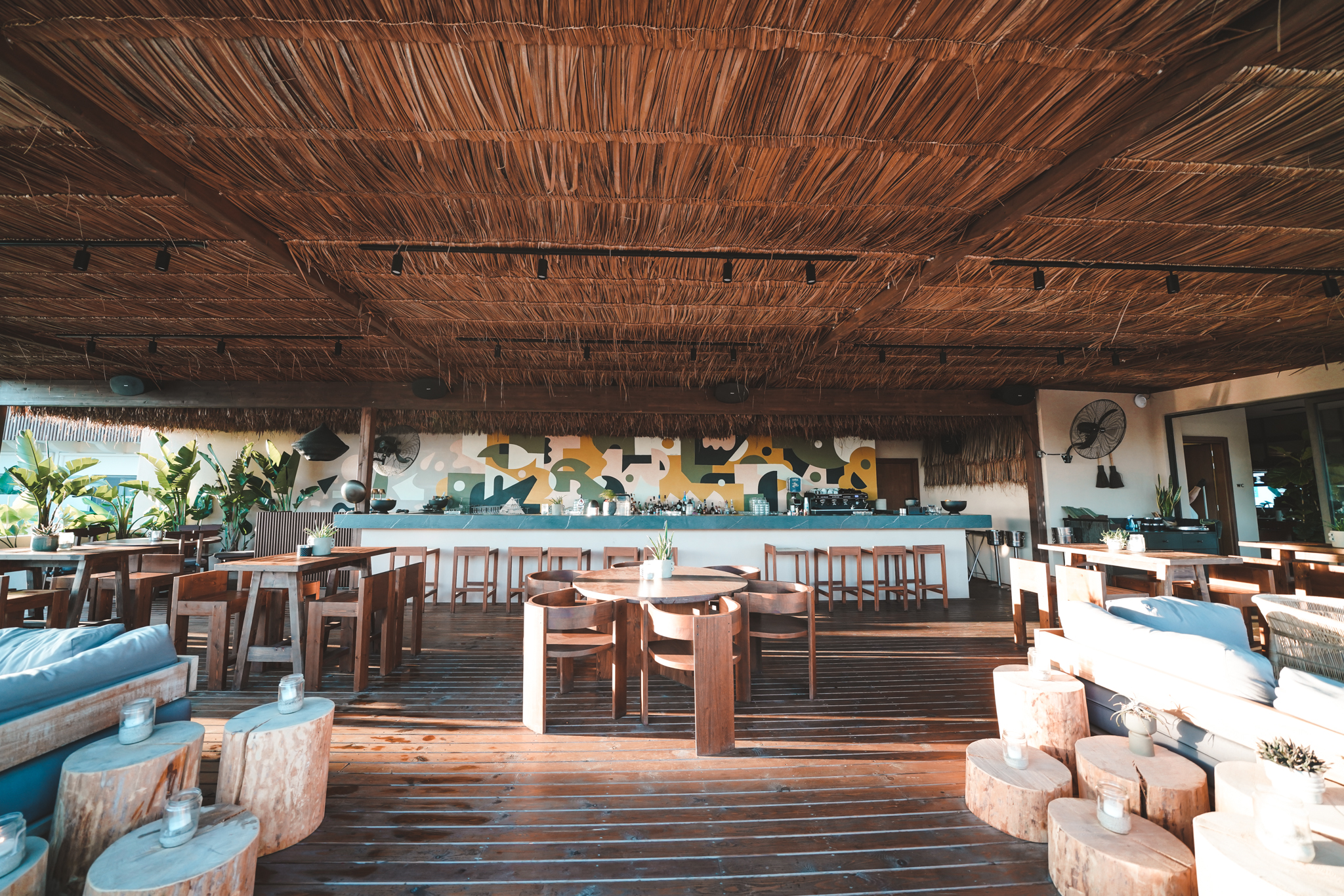 Offene Strandbar mit Holzmöbeln, Strohdach und modernem Wanddesign, das eine entspannte Urlaubsatmosphäre schafft.