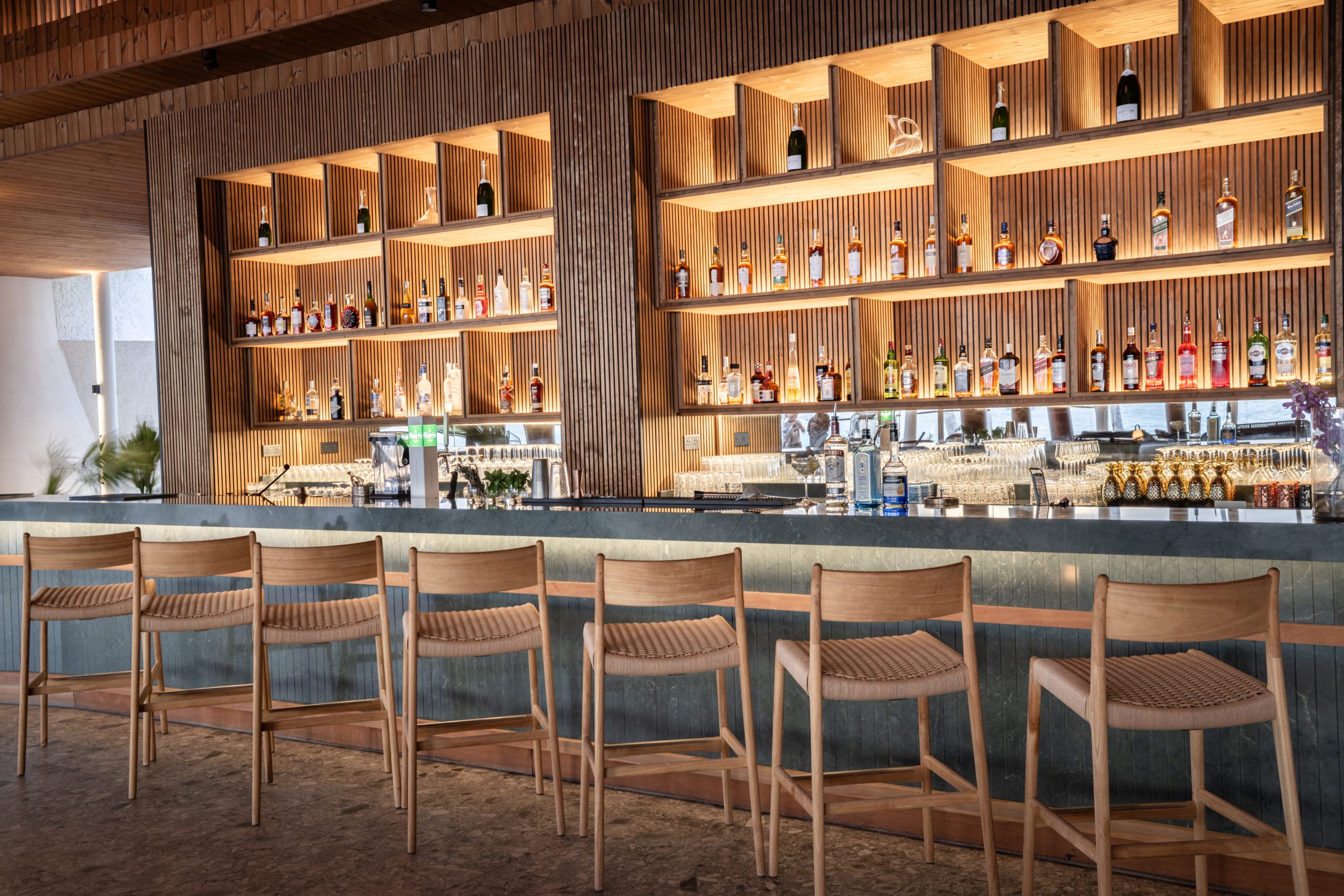„Stilvolle Hotelbar mit moderner Holzeinrichtung, hohen Barhockern und beleuchteten Regalen voller Spirituosen und Champagnerflaschen.“
