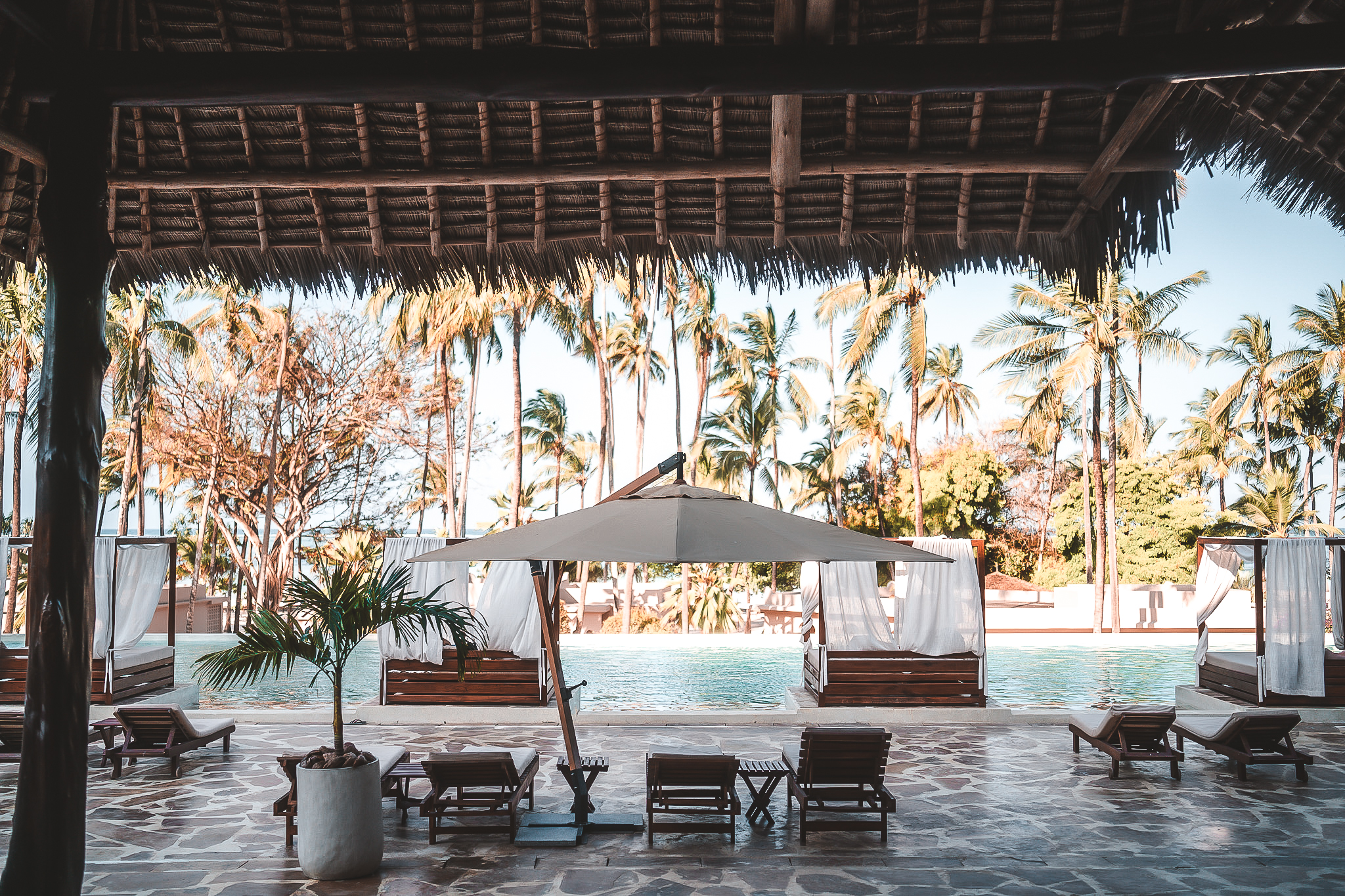 Luxuriöse Pool-Lounge mit Sonnenliegen und Bali-Betten unter Palmen.