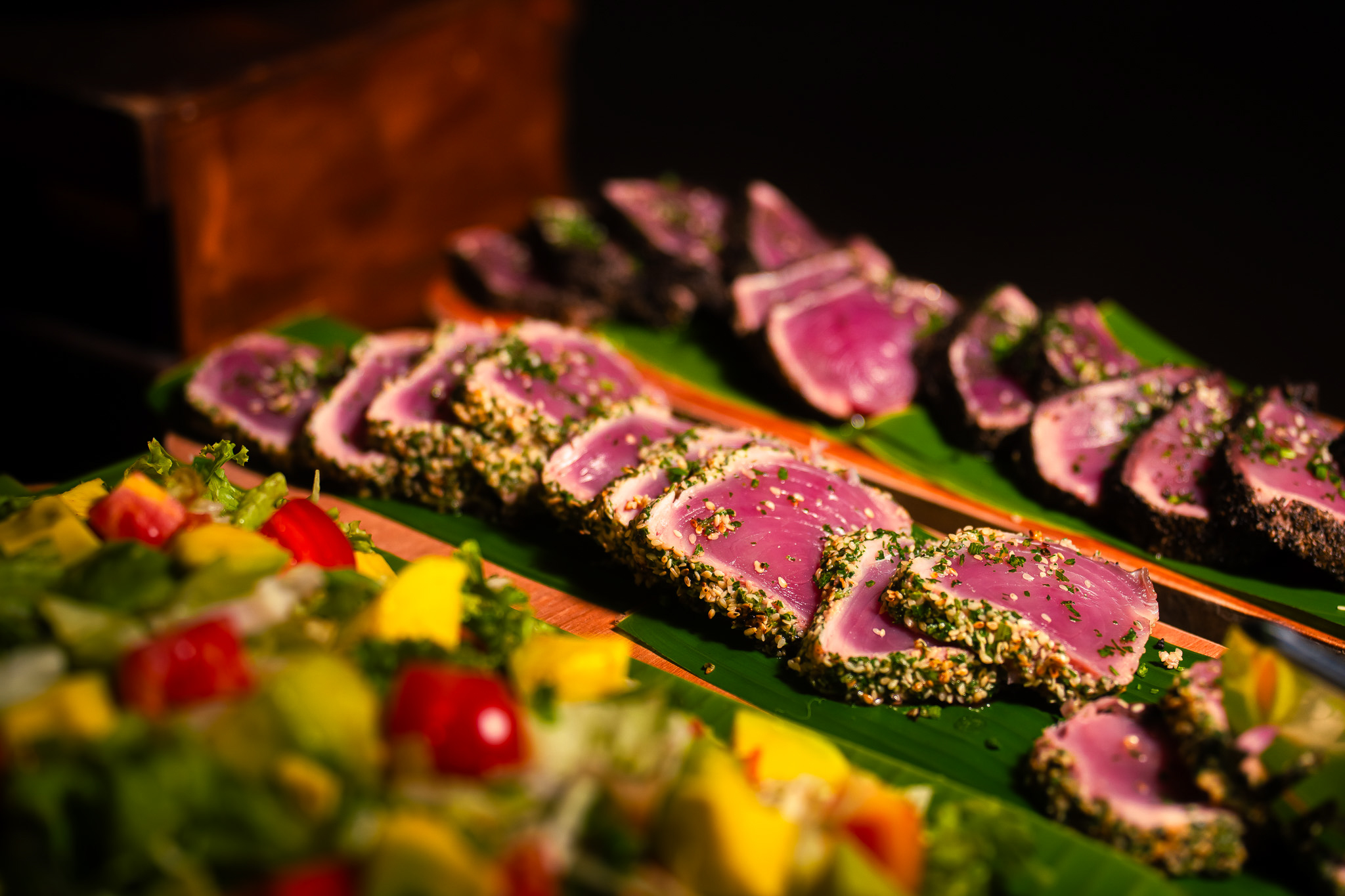 Frisch aufgeschnittener, rosa Thunfisch mit Sesamkruste, serviert auf Bananenblättern mit buntem Salat.