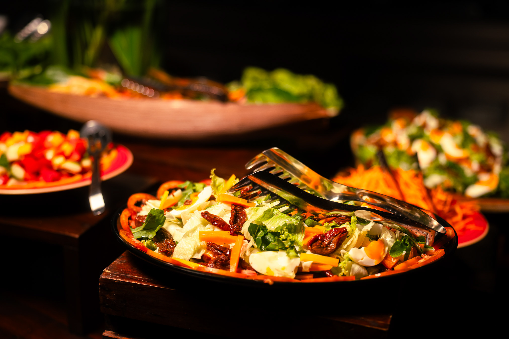 Frischer bunter Salatteller mit Tomaten, Karotten, Eiern und Kräutern, serviert am Buffet mit weiteren bunten Speisen im Hintergrund.