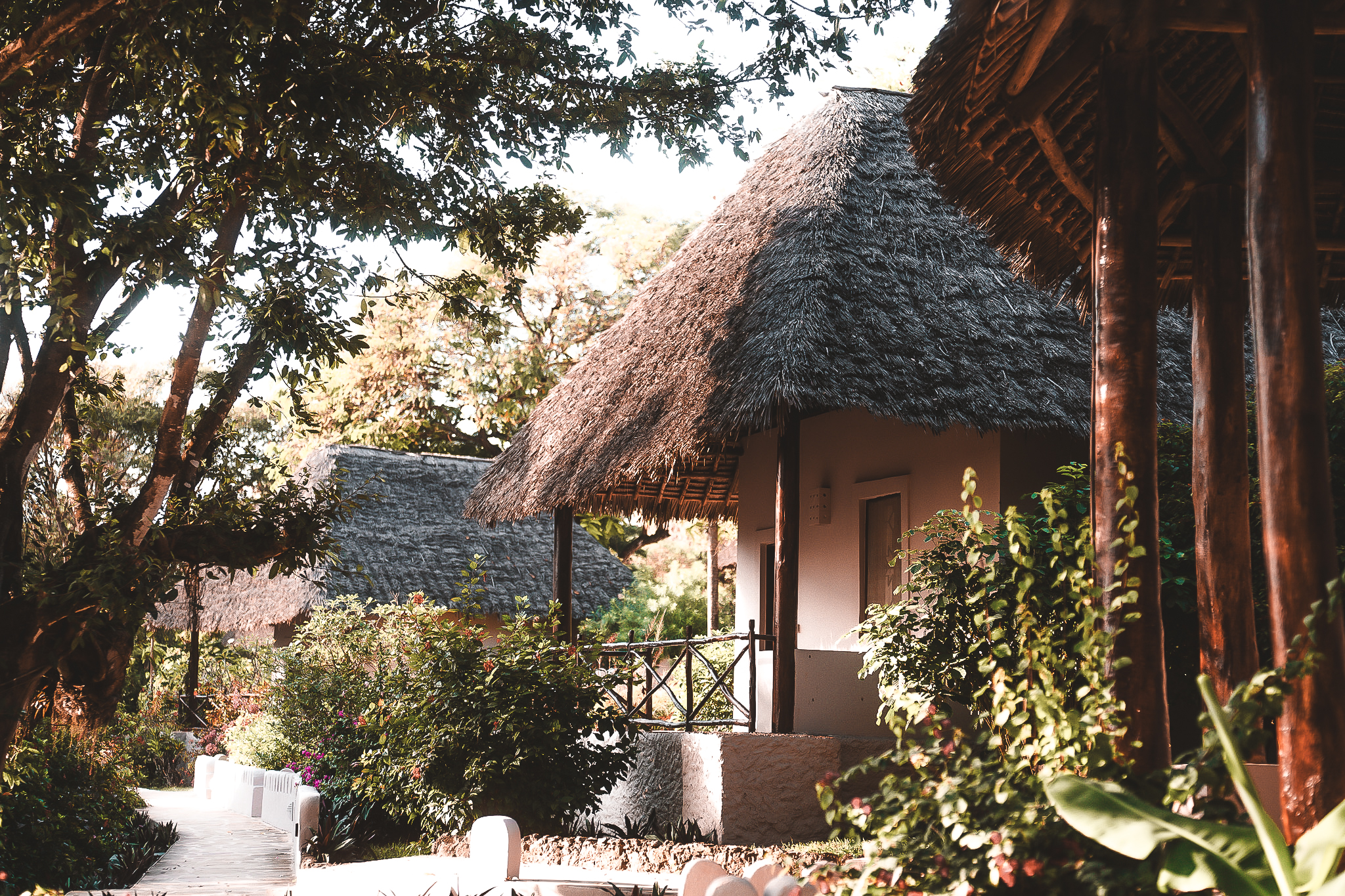 Traditionelle Bungalows mit Strohdächern im Diamonds Mapenzi Zanzibar, umgeben von tropischer Vegetation und Gartenwegen.