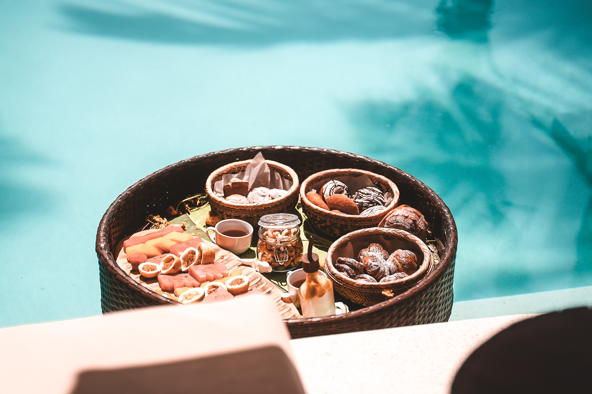 Schwimmendes Frühstückstablett im Pool, gefüllt mit exotischen Früchten, Gebäck, Nüssen und Kaffee.