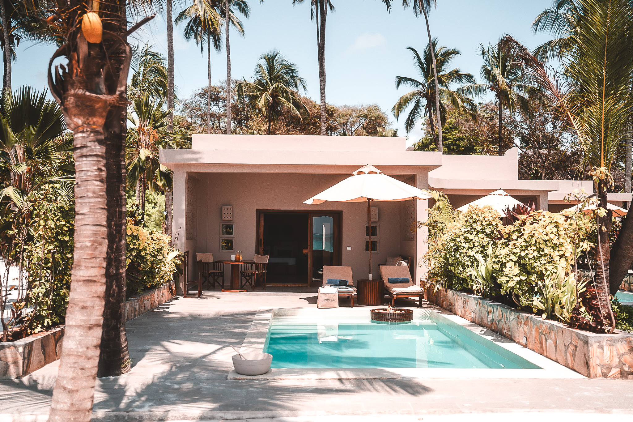Private Villa mit eigenem Pool, Sonnenliegen und Sonnenschirm, umgeben von tropischer Vegetation und Palmen.